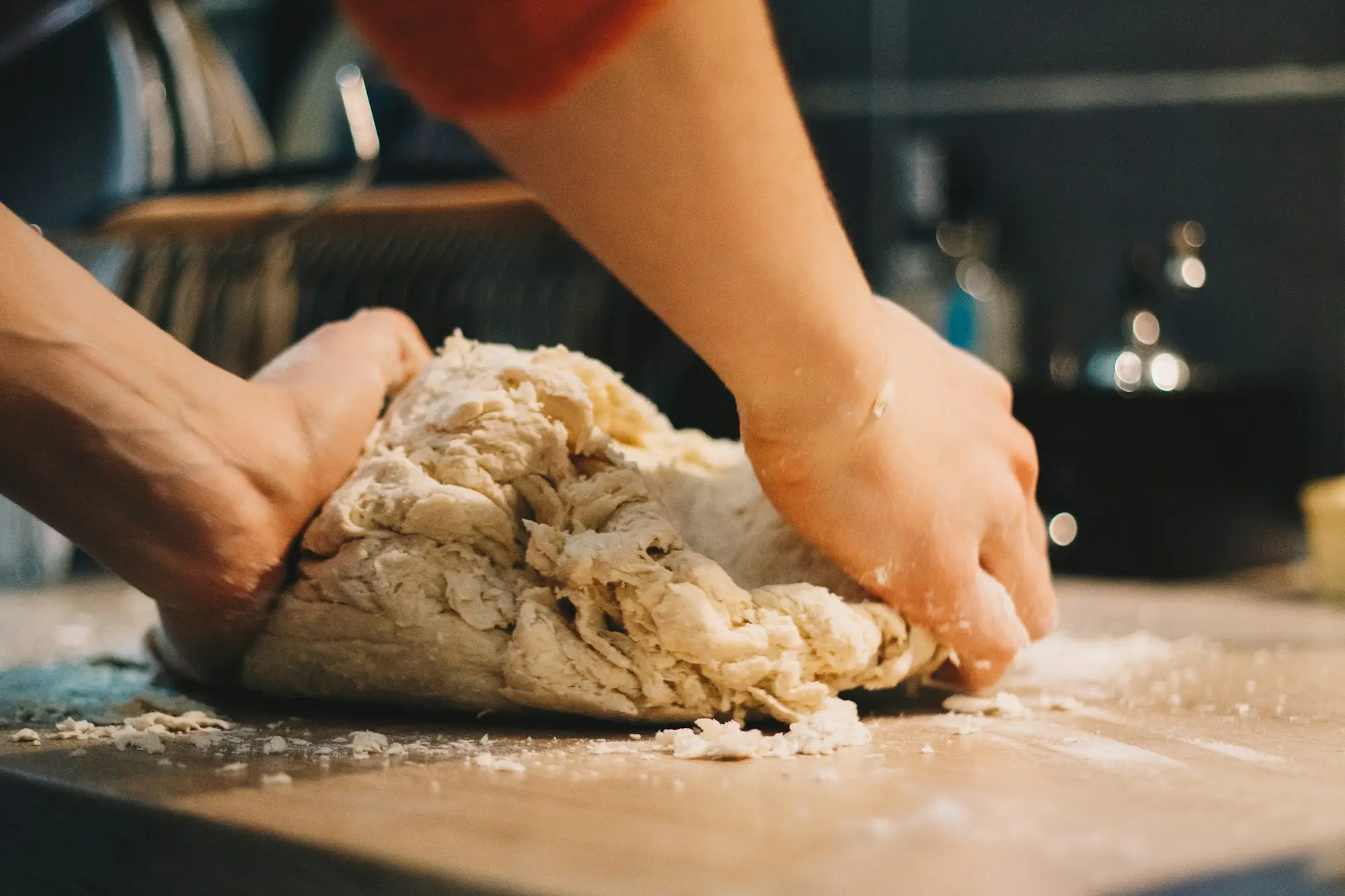 Floury hands kneading dough on a wooden bench in warm light.
