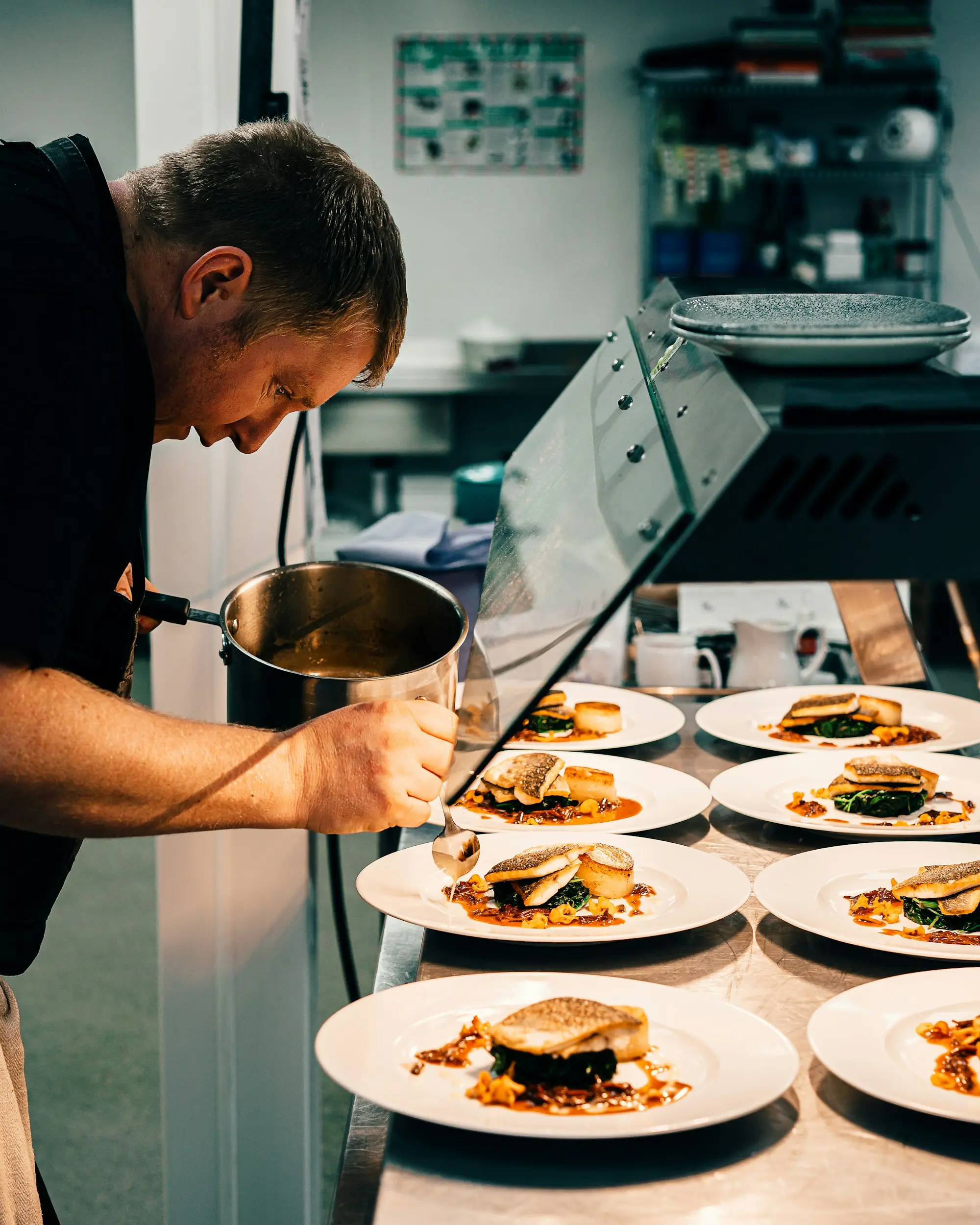 A chef plating several dishes during a busy restaurant service in a commercial kitchen.